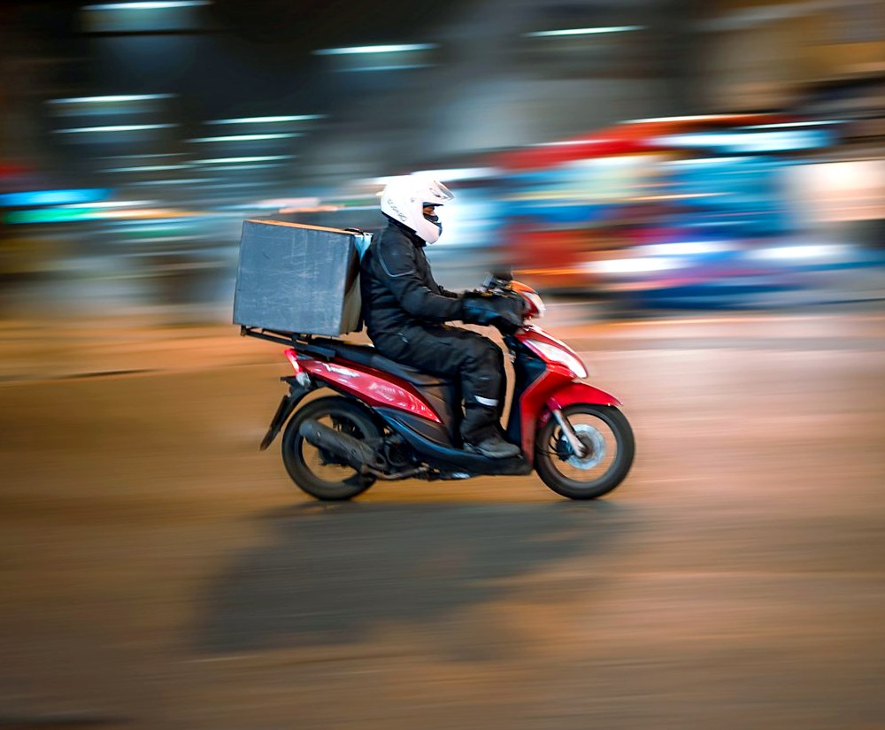 Mensajero en motocicleta recorriendo la ciudad con un paquete